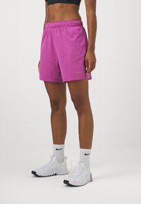 Pantalones cortos rosas de Nike con cintura elástica, combinados con zapatillas deportivas blancas y azul claro y calcetines grises de Nike. Textura suave.
