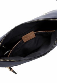 Innenseite einer marineblauen Tragetasche mit goldenem Reißverschluss, beigem Futter und einem kleinen Lederschild. Glatte Textur und schlichtes Design, ideal zur Organisation.