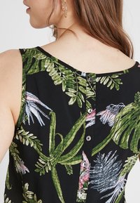 Top sin mangas negro con un diseño de follaje verde y patrones florales en rosa, con escote en V y cinco botones en la parte posterior para el cierre.