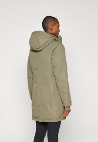 Olijfgroene parka met een capuchon, getailleerde pasvorm, gewatteerd ontwerp en gestikte naden. Beschikt over lange mouwen en een lengte tot halverwege de bovenbenen.