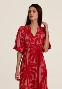 Robe à imprimé floral rouge avec un décolleté en V et de courtes manches bouffantes. Fabrication en tissu léger présentant des motifs de feuilles de palmier.