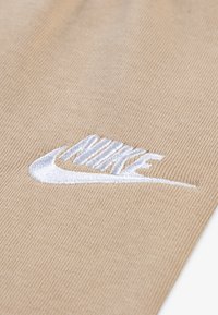 Bežna tkanina s teksturiranim pletenim uzorkom. Sadrži istaknuti bijeli vezeni Nike logo. Dizajn je elegantan i minimalistički.