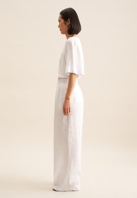 Witte linnen twee-delige outfit bestaande uit een losse top met korte mouwen en brede broekspijpen, die op de taille wordt vastgezet met een bijpassende riem.