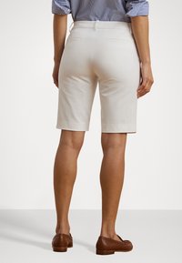 Knee-långa beige shorts i bomull, med en mjuk textur, två bakfickor och kombinerade med bruna platta skor.