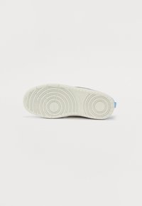 Semelle de chaussure en caoutchouc blanc texturé, avec des motifs circulaires, des stries et un onglet de talon bleu pour une meilleure adhérence et flexibilité.