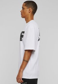 Balsakains balts kokvilnas T-krekls ar īsām piedurknēm, kuram ir izteikts melns grafiskais prints gan priekšā, gan aizmugurē, piedāvājot brīvu piegriezumu.