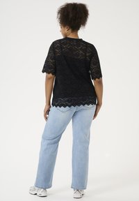 Black lace t-shirt with short sleeves, scalloped hem, and floral pattern, worn with light blue jeans and gray athletic shoes.