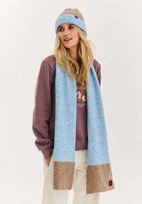 Modrá a hnědá pletená čepice a šála s měkkou texturou, modrá šála s hnědým akcentem na spodní části a detaily s logem.