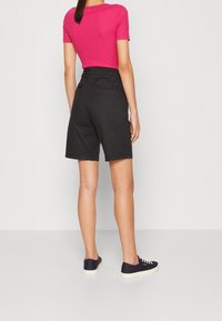 Zwarte shorts met een getailleerde taille, gemaakt van gladde stof. Gecombineerd met een felroze top met korte mouwen en donkere sneakers.