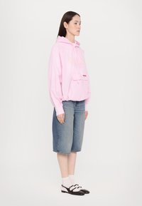 Rosa karierte Übergröße-Hoodie mit einer Fronttasche, kombiniert mit blauen Denim-Bermuda-Shorts und schwarz-weißen zweifarbigen Schuhen.