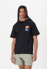Sort bomulds t-shirt med et multicolor grafisk design, der skildrer en solnedgang og glas, korte ærmer og en afslappet pasform.