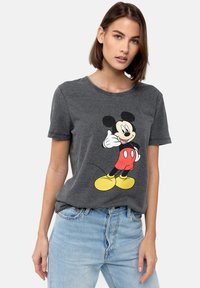 Harmaa puuvillapaita, jossa on suuri Mickey Mouse -grafiikka mustana, punaisena ja keltaisena. Pyöreä kaula-aukko ja lyhyet hihat, rento malli.