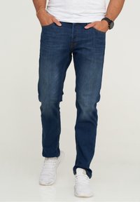 Mörkblå denimjeans med slim fit, med en urtvättad look, femficksdesign och kontrasterande orange sömmar, bärs med vita sneakers.