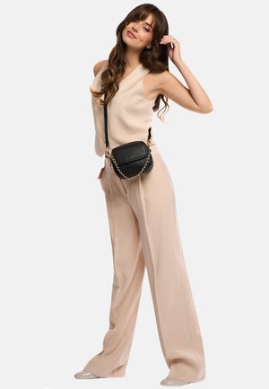 Borsa a tracolla nera con superficie testurizzata, dettagli in catena dorata e forma rettangolare, abbinata a un top beige senza maniche e pantaloni larghi.