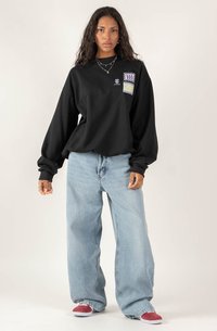 Czarna, oversize bluza z długimi rękawami i kolorowymi grafikami naszytymi. W połączeniu z jasnoniebieskimi, luźnymi dżinsami i czerwonymi butami wsuwanymi.