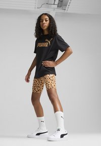 T-shirt nera con logo in stampa leopardata oro, abbinate a pantaloni corti con stampa leopardata, calzini bianchi e scarpe bianche con dettagli neri.