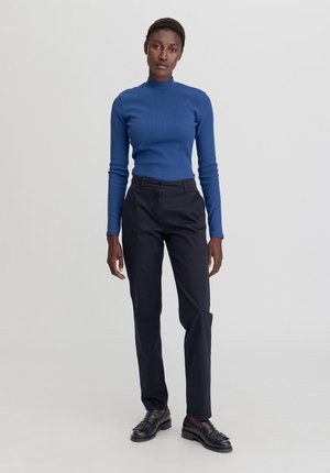 Top azzurro aderente a maniche lunghe abbinato a pantaloni neri slim e mocassini neri. Texture liscia, design semplice e sfondo neutro.