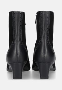 Zwarte enkellaarsjes van een mix van leer en wildleder met decoratieve uitsparingen en stiksels, met een lage hak en een ritssluiting aan de achterkant.