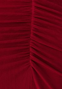 Raudonos audinio suknelė su vertikaliais raukšlėjimo akcentais. Lygus paviršius ir subtilus blizgesys. Prisekamas siluetas su švelnia drapiruote per kūną.