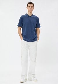Marineblå polo T-shirt med en blød tekstur og krave, parret med hvide cargo bukser med sidelommer og en afslappet pasform. Hvide sneakers.