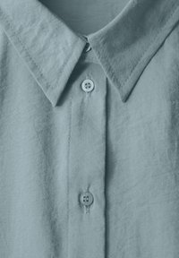 Camicia azzurro chiaro, con bottoni, realizzata in tessuto testurizzato, caratterizzata da un colletto classico e una fila centrale di bottoni con un accento cucito.