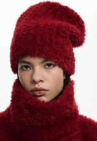 Pălărie roșie din blană artificială, cu vârf rotunjit și guler înalt asortat, având o suprafață moale și texturată și un aspect confortabil.