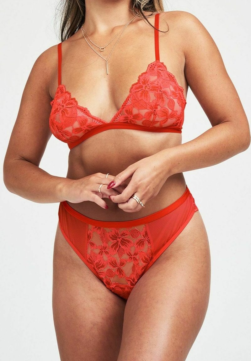 Reggiseno in pizzo rosso e slip alta vita abbinati con motivi floreali, pannelli trasparenti e spalline regolabili. Texture morbida e design aderente.