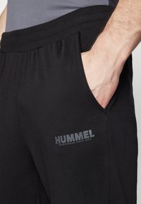Svarta Hummel sweatpants med en ribbad midja och sidofickor. Har en grå logotryck på vänster lår. Mjukt, stretchigt tyg.