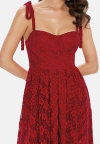 Abito rosso in pizzo con busto aderente, gonna ampia, spalline regolabili e motivo floreale in pizzo. Texture liscia e design a strati.