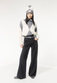 Strickpullover mit grau-weißen Rautenmuster, kombiniert mit hochgeschnittenen schwarzen Jeans. Eine passende Mütze rundet den Look ab.