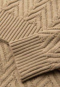 Maglione lavorato a maglia beige con un motivo a spina di pesce testurizzato e polsini a costine. Il materiale sembra morbido ed elastico. Evidente maestria artigianale.