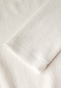 Witte textuurstof met een geribbeld patroon, met een gevouwen hoek die een zachte, geweven textuur toont.