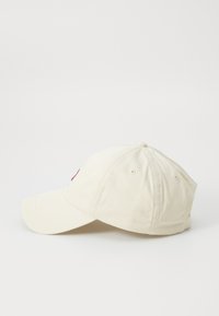 Beige caps med buet br brim, laget av bomull, med broderte detaljer foran og ventilasjonsåpninger på sidene.