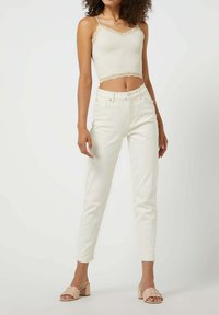 Witte denim jeans met een slim fit, gecombineerd met een beige crop top met kantafwerking. Model draagt lichte tan blokhak sandalen.