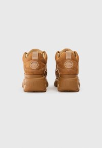 Tan semišové vysoké tenisky s polstrovanými goliermi, zaoblenými šnúrkami a textúrovanými gumovými podrážkami. Na päte sa nachádza okrúhle logo.