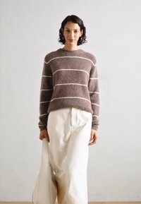 Braun gestreifter Pullover aus weichem Strickstoff, kombiniert mit weißen weit geschnittenen Hosen. Einfaches Design mit Rundhalsausschnitt und lockerer Passform.