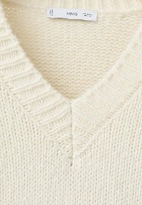 Maglione a V crema con lavorazione a trame, con bordi a costine. Realizzato in filato morbido, presenta un design semplice e accogliente.