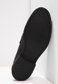 Sola de sapato preta com um design de borracha texturizada, apresentando uma borda limpa e uma marcação subtil. A forma é plana com uma superfície flexível.