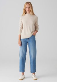 Beige sweater with ribbed accents, paired with blue straight-leg jeans and white sneakers. Light texture with a relaxed fit and side slit.
