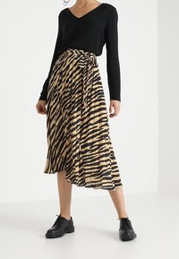 Haut noir à manches longues associé à une jupe portefeuille rayée beige et noire longueur genou. Complété par des chaussures noires à lacets.