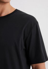 Schwarz kurzärmliges T-Shirt aus weicher Baumwolle mit Rundhalsausschnitt und minimalen Nähten an den Ärmeln.