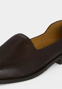 Σκούρο καφέ παπούτσι loafer με υφή φιδιού και ταμπά δερμάτινη επένδυση, εμφανιζόμενο από πλάγια γωνία.