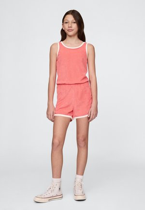 Koraltowy kombinezon z frotté z białą lamówką, posiadający bezrękawnik i spodenki z elastycznym pasem. W połączeniu z białymi wysokimi trampkami.