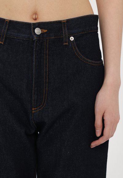 I jeans in denim scuro presentano cuciture arancioni e una chiusura con bottone, con tasche frontali e una vestibilità dritta, che mettono in mostra una texture liscia.