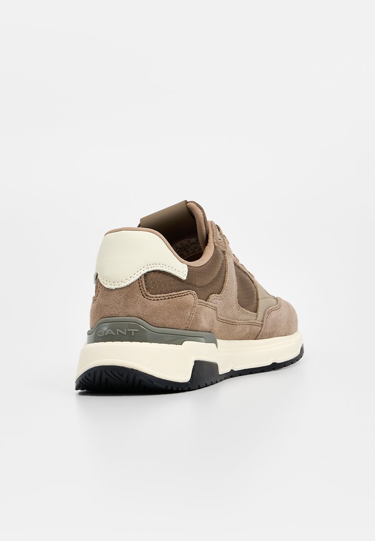 Baskets en daim marron avec une semelle épaisse noire et blanche, des accents crème et un col rembourré. Présente un logo au niveau du talon et des panneaux texturés.