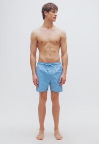 Ανοιχτό μπλε μαγιό σορτς με ελαστική μέση και κορδόνι. Λείο υλικό, μήκος έως το γόνατο, σχεδιασμένο για άνεση και ευκολία κινήσεων.