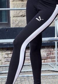 Crne tajice s bijelim bočnim prugama, s Puma logotipom na bedru. Napravljene od rastezljivog materijala za udobnost i fleksibilnost.