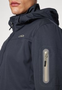 Navy blue waterproof jacket with a textured finish, adjustable hood, and side pocket with a contrasting zipper detail. CMP logo on chest.