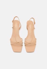 Γυμνές ψεύτικες δερμάτινες σάνταλες slingback με τετράγωνη μύτη και λεπτές ράβδους. Διαθέτουν χαμηλό τακούνι και μινιμαλιστική σχεδίαση. Λεπτομέρεια με χρυσό τόνο.