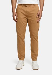 Trousers in light brown cotton fabric, slim fit with a smooth texture, featuring belt loops and side pockets, paired with white sneakers.